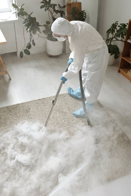 A person using a vacuum cleaner with a yellow body and a black hose attachment to deep clean a patterned area rug in a residential room. The individual, dressed in casual clothing including jeans, whi